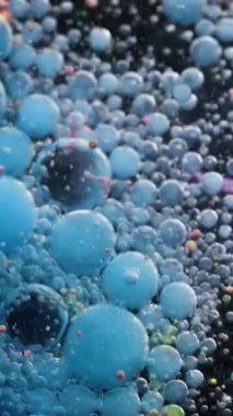 Dikey video. Akrilik baloncuk. Fizzy sıvısı. Mavi, siyah, köpüklü, mürekkepli su akışı. Patlayan yağ parçacıkları renk damlaları soyut arkaplanı bulanıklaştırır.