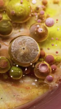 Dikey video. Fizzy sıvısı. Köpük dokusu. Bulanık sarı, altın sarısı, pırıl pırıl parlayan boya emülsiyonu yuvarlak, soyut su arka planında yüzen damlacık..