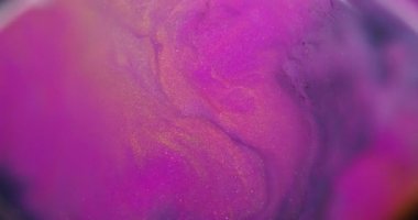 Bulanık boya dökülüyor. Parlak pigmentler. Soyut arkaplana yayılan mor pembe altın renkli simli partiküller..