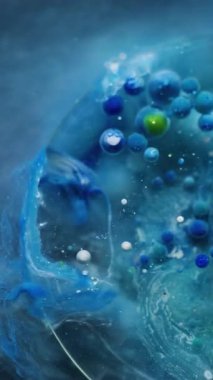 Dikey video. Boya akışı. Mürekkep su kabarcığı. Çemberin şeffaf renk damlaları mermer mavisi gri sıvı yüzeyde yüzer. Jel parçacıkları soyut arkaplan.