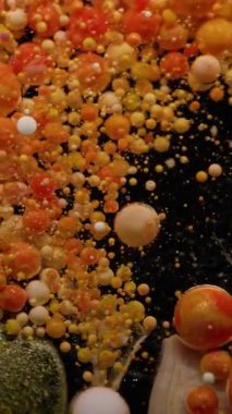 Dikey video. Köpüklü sıvı. Boya balonu patladı. Siyah suya dökülen parlak, yuvarlak parçacıklar. Turuncu damla pigmenti patlayan soyut arkaplan.