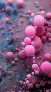 Dikey video. Yağ sıvısı. Su damlasını boya. Bulanık pembe gri mavi şeffaf kabarcıklar suda yüzüyor. Patlayan jel dokusu serumu soyut sanat arkaplanı.