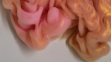 Boya fırıldağı. Renk bulutu. Odaklanamayan pembe, altın sarısı, akrilik, simli duman dokusu soyut beyaz arka planda yükseliyor..