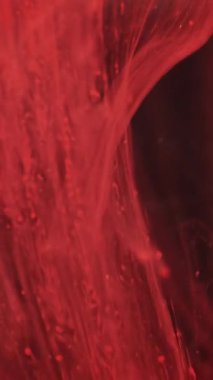 Dikey video. Bulanık akış. Su damlayan boya. Odaklanmamış kırmızı renk parlaklık sıvısı soyut sanat arkaplanı üzerine duman dokusu dalgası düşürür..