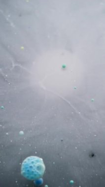 Dikey video. Boya çiçeği. Renk patlaması. Siyah su yüzeyine yayılan beyaz mürekkep damlası sisi yağ jeli baloncukları. Sanat açıcı soyut arkaplan.