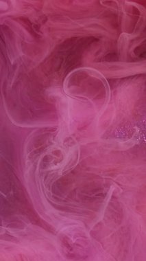 Dikey video. Boya su sıçratır. Görüntü arka planda parıldıyor. Odaklanamayan pembe renkli, parlayan mürekkep dumanı deseni soyut sanat ışığı üzerinde yüzüyor.