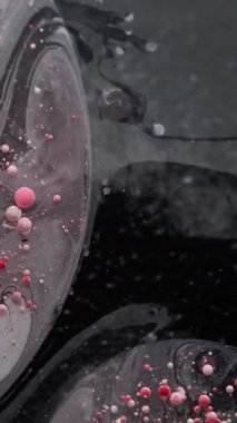 Dikey video. Yağ pigmenti düşüyor. Kabarcık emülsiyonu. Kırmızı beyaz boya parçacıkları patlayan yüzey suyu döküyorlar. Sakinleştirici dalga, sıvı koyu arkaplanı karıştırıyor..