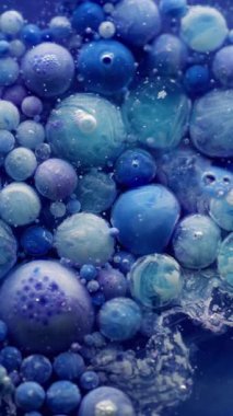 Dikey video. Boya jeli. Yağ kabarcıkları. Mavi boya damlaları küçük parçacıklarla renkli sıvıda akıyor. Yaratıcı sıvı karışımı soyut arka plan köpük yüzeyi.