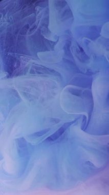 Dikey video. Boya dumanı. Soyut dumanlı. Odaklanmamış mavi pembe renk parıldıyor. Işıldayan sanat ışığı arka planında yüzen mürekkep dokusu sisi sıçrıyor..