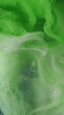 Dikey video. Bulut dumanı. Mürekkep suyu. Odaklanmamış yeşil beyaz renkler parıldıyor. Parlayan soyut sanat ışığı arka planında boya deseni sisi yüzüyor..