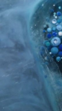 Dikey video. Mermer yağ damlası. Duman sıvısı. Yüzeyde hareket eden büyük şeffaf nokta jel kabarcıkları çözünmüş sisli su üzerinde hareket ediyor. Mavi gri köpük soyut arkaplan