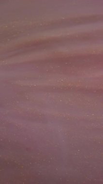 Dikey video. Boya akışı. Işıldayan sıvı. Pembe şeftali rengi değişen mistik parlak kıvrımlı mermer çıkarılmış soyut arkaplan.