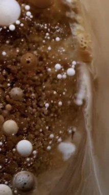 Dikey video. Baloncuk döküldü. Boya karışımı. Yağ rengi hipnoz yoluyla suda çözünür. Kahverengi bej beyaz pigment patlaması soyut sanat arkaplanı sıçratıyor.