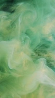 Dikey video. Parıldayan duman. Mürekkepli su sıçraması. Odaklanmamış yeşil altın rengi parlak desen sisi yayılan girdap hareket eden soyut sanat arkaplanı.