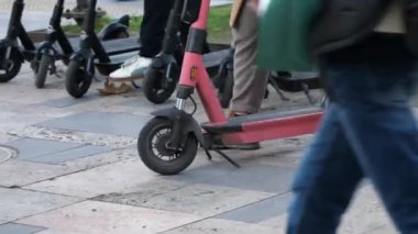 İnsanlar scooter parkından elektrikli scooter alıp gezintiye çıkıyorlar. Şehirdeki kiralık e-scooterlara binmeye başlayan erkeklerin diz üstü çekimleri.. 