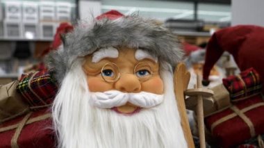 Altın gözlüklü, beyaz sakallı, tahta gökyüzü tutan mutlu Noel Baba bebeği. Gülümseyen Noel Baba 'nın yakın plan portresi mağazanın raflarında ve yürüyen insanların arka planında. Noel süslemesi