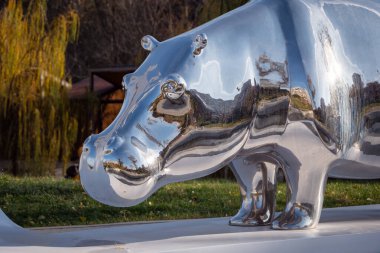 Krom hipopotam heykelinin ayrıntıları beyaz bir kaide üzerinde duruyor, yeşil çimenler ve ağaçların arka planında. Tiflis, Gürcistan - 04 Aralık 2023.