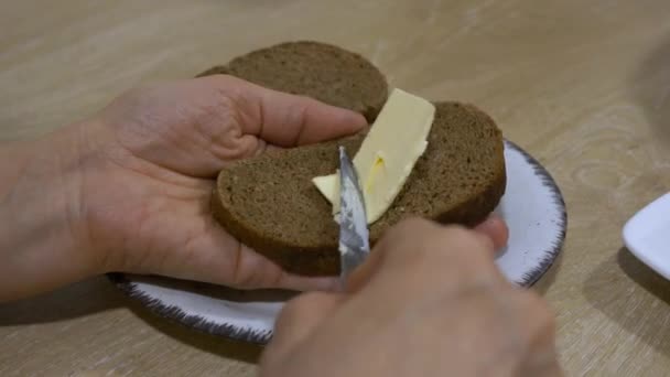 一个人用小刀在白盘上的一片黑面包上顺利地撒满黄油 细述了一个简单的日常厨房任务 高角度的中景 — 图库视频影像