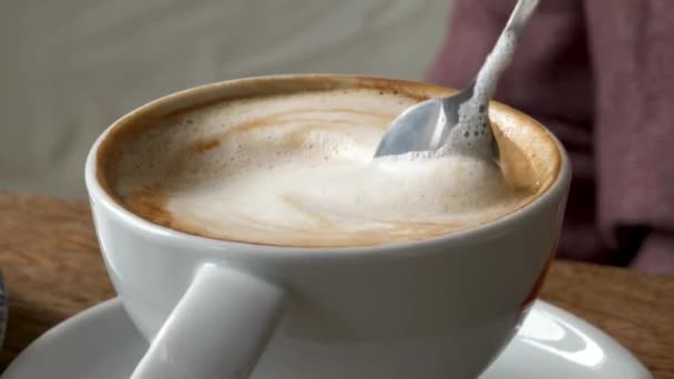 素朴な木製のタブレットに銀のスプーンで白い陶磁器のコップでカプチーノコーヒーをかき混ぜる手 クローズアップショット — ストック動画