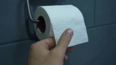 Birisi bir tuvalet kağıdını bir eliyle, tuvalet kağıdına monte edilmiş bir rulo kağıdı kendine güvenle çekiyor..