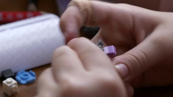 一个受伤的孩子 他的手指受伤了 他用五颜六色的塑料零件在一张木制桌子上组装了一个玩具 — 图库视频影像