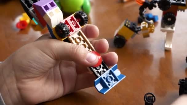 一个男孩在一张木制桌子上拆卸一辆五颜六色的汽车 这辆车是用相互关联的塑料建筑玩具立方体制造的 可以近距离看到双手 — 图库视频影像
