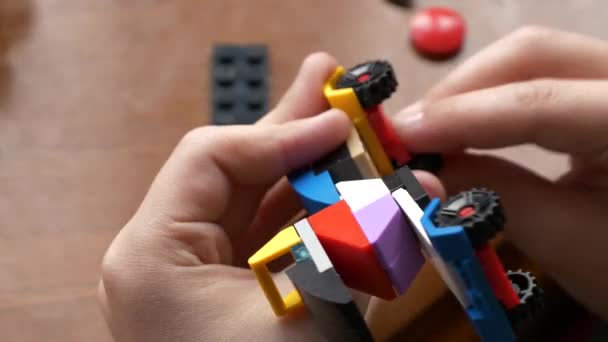 木のテーブルにプラスチック製の建設のおもちゃキューブを連結して作られたカラフルな車を組み立てる子供の手のクローズアップビュー — ストック動画