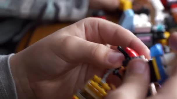 木のテーブルのプラスチック構造の部品を連結することから成っている多彩なおもちゃ車を組み立てている子供の手のクローズアップビュー — ストック動画