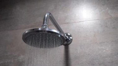 Yuvarlak, gümüş renginde bir duş başlığından aşağı su akıyor fayanslarla döşenmiş banyo duvarına yakın çekim görüntüsünde..