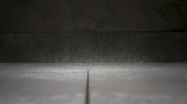 Duş damlacıkları beyaz fayanslı banyo zeminine düşüyor ve zemin seviyesinde su sıçramaları yaratıyor..