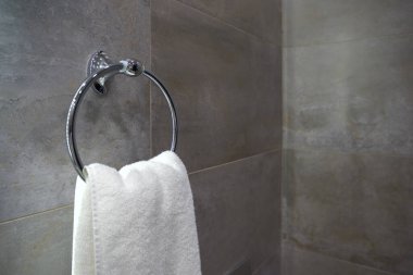 Zarif gri kiremitli banyo duvarında parlak metal bir havlu halkasına asılı beyaz bir havlu..