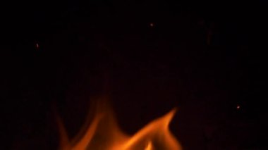 Karanlığın içinde titreyen parlak alevlerin yakın planında karanlık bir zemin var..