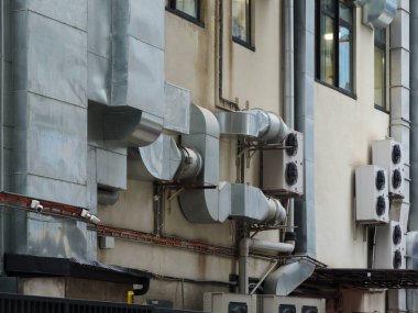 Metal havalandırma kanalları ve havalandırma ünitelerinden oluşan karmaşık bir yapıya sahip bir binanın dış görüntüsü..