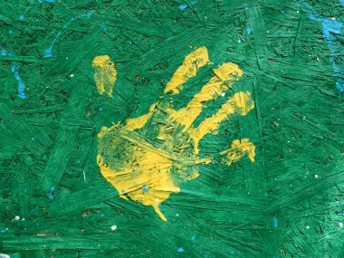 A single yellow handprint stands out on a textured green painted wooden surface, creating a striking contrast and evoking a sense of creativity and spontaneity.