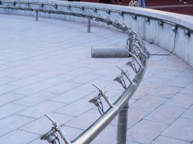 Şehir meydanındaki kuru, dairesel bir çeşme havzası su püskürtme başlıklarını ve ışık sistemini kenarı boyunca monte eder..
