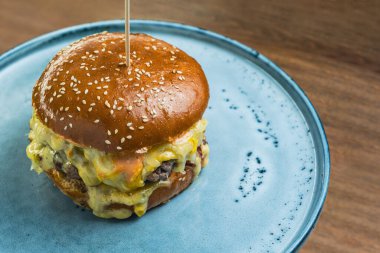 Eritilmiş peynirli çizburger ahşap bir masa yüzeyinde büyük bir tabakta servis edilir, yüksek açılı yakın çekim..