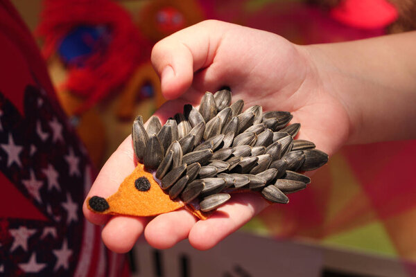Крупный план детской руки с игрушкой из ёжика ручной работы, сделанной из семян подсолнуха.