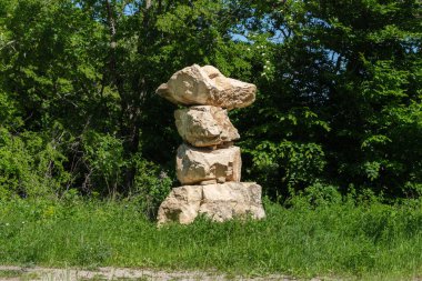 Bir ormanda, yoğun yeşil yapraklarla çevrili, açık renkli, eskimiş kaya parçaları yığını..