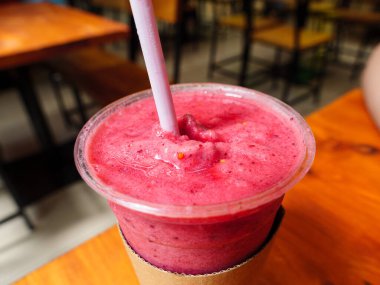 Pembe smoothie, şeffaf plastik bir bardakta pipetle bir kafedeki ahşap masada oturuyor, yakın çekim..