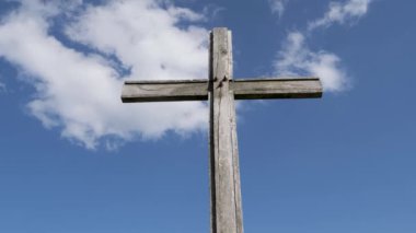 Yıpranmış ahşap bir haç, tüylü beyaz bulutlu parlak mavi bir gökyüzüne karşı dimdik ayakta duruyor. Haç inancın ve umudun sembolüdür..