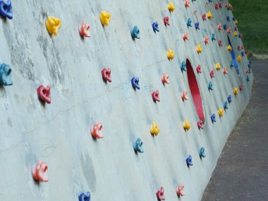 A concrete climbing wall for children in a park, with various colored handholds and a red circle cutout. clipart