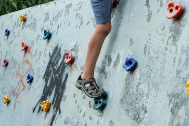 Genç bir çocuk bir parkta tırmanma duvarına tırmanıyor. Çocuğun ayağı tutunun..