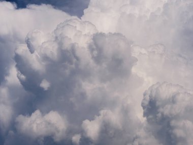 Kabarık, beyaz kümülüs bulutları açık mavi gökyüzüne karşı. Bulutlar yumuşak ve dalgalı, değişik şekil ve boyutlarda..