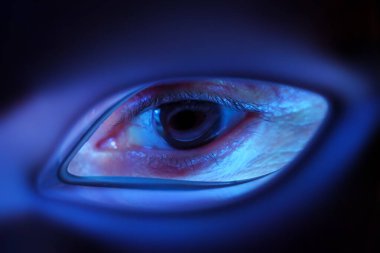 Bir kadının gözü ışık terapi maskesinden görülür. Maskeden gelen mavi ışık, yakından bakınca gözü aydınlatır..