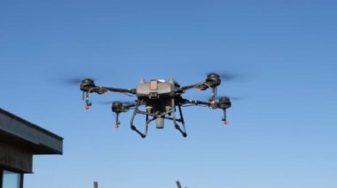 Binanın yakınında, açık mavi gökyüzüne karşı uçan böcek ilacı püskürtücü dron. İnsansız hava aracının dört pervanesi, bir sprey tankı var ve sprey ilaçlama uygulaması için enjektörlerle donatılmış..