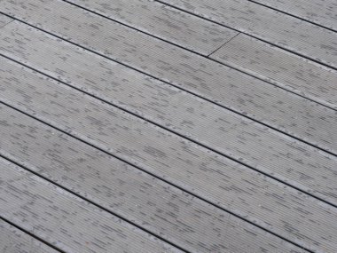 Ahşap güverte zemini yeni yağan yağmurdan sonra ıslak, gri tahtaları gösteriyor. Tahta taneleri ve su damlacıklarının deseni görülebilir..