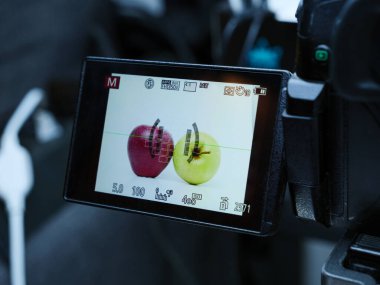 Stüdyoda profesyonel bir kamera ekranında kırmızı ve sarı bir elma görüntüler. Kamera manuel modda çekiyor ve odak noktası görünür..