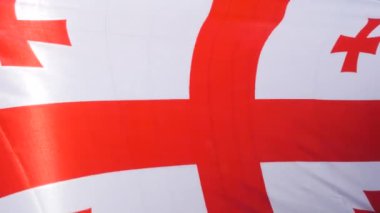 Gürcistan bayrağı rüzgarda zarif bir şekilde dalgalanıyor, canlı renklerini ve belirgin tasarımını sergiliyor. Bu açık hava ortamında gurur ve kültürel öneme sahip bir anı yakalar..