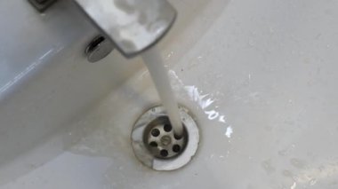 Musluktan sürekli olarak lavaboya akan su, rutin bir ev aktivitesini gösteren yerleşim ortamında musluğun açıldığını gösteriyor..