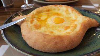 Yeni pişmiş bir Adjarian Khachapuri tabakta servis edilir, içi kabuklu ve yumurtalı vıcık vıcık peynirli.